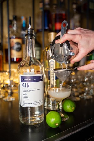 Bartender fine-straining a gin cocktail into a coupe