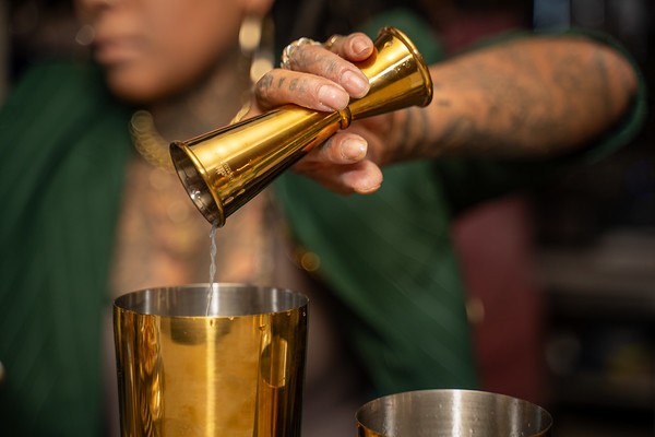 Bartender measuring a pour with a gold jigger